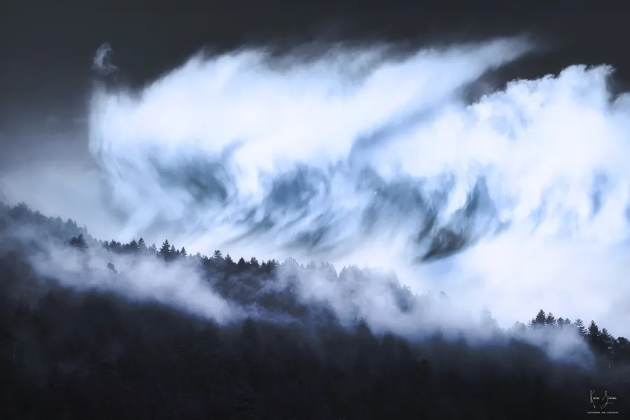 Des nuages roulent au-dessus d’une forêt de montagne